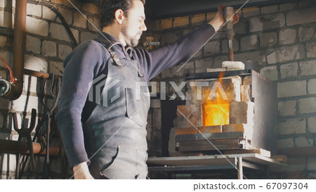 Blacksmith regulates the fire in the furnace with hot metal 67097304