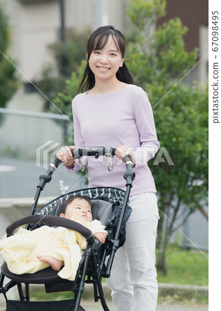 Mother and baby boy pushing a stroller and walking in a residential area 67098495