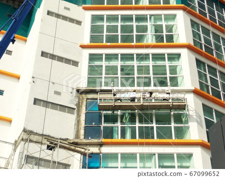 KUALA LUMPUR, MALAYSIA -MARCH 16, 2017: Workers are in the process of cleaning and maintenance exterior the building by using a service gondola. They are wearing a safety harness as a safety measure. 67099652