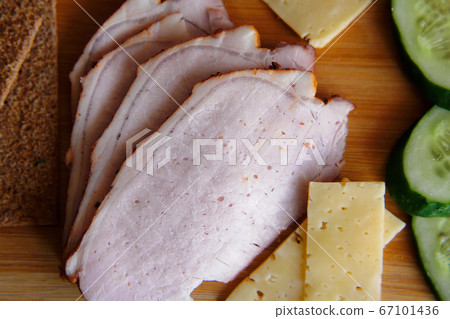 Slicing ham, cucumbers and cheese with ruddy thin breads lie on a wooden board. Slicing ham, cucumbers and cheese with ruddy thin breads lie on a wooden board. 67101436
