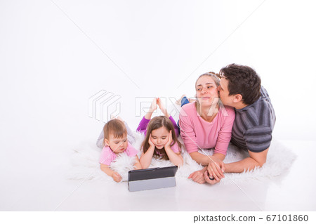 the kids are watching cartoons on the tablet. a man and a woman embrace. Family vacation, joint pastime. Parents with girls on the floor the kids are watching cartoons on the tablet. a man and a woman embrace. Family vacation, joint pastime. Parents with girls on the floor 67101860