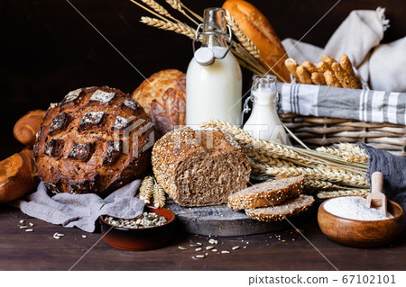 Concept of homemade bread, natural farm products, domestic production. Healthy and tasty organic food. Cut bread, milk, flour. Wheat spica as decor. Closeup, dark wooden background 67102101