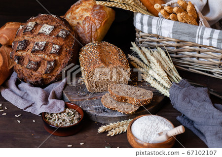 Concept of homemade bread, natural farm products, domestic production. Healthy and tasty organic food. Cut bread, milk, flour. Wheat spica as decor. Closeup, dark wooden background 67102107