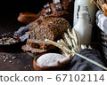 Concept of homemade bread, natural farm products, domestic production. Healthy and tasty organic food. Cut bread, milk, flour. Wheat spica as decor. Closeup, dark wooden background 67102114
