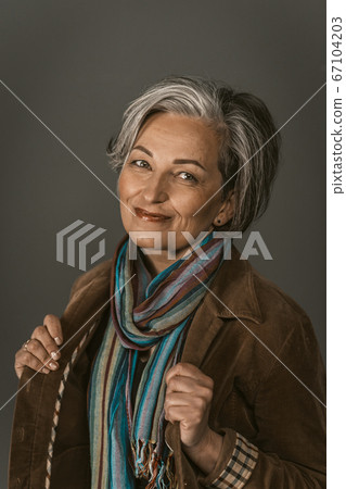 Smiling mature woman in casual. Female portrait on gray. Lady wearing colorfull scarf and jacket smiles looking at camera. Tinted image 67104203