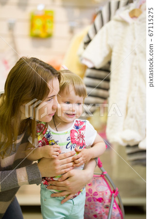 Young woman and her daughter smiling at the children's clothes shop Young woman and her daughter smiling at the children's clothes shop 67115275