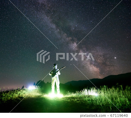 Space traveler playing guitar under beautiful starry sky. 67119640