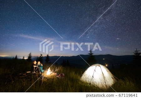 Friends travellers spending time in the mountains sitting around bonfire in camping under beautiful starry sky 67119641