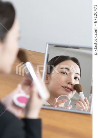一個年輕的女人，在鏡子裡化妝 67120473