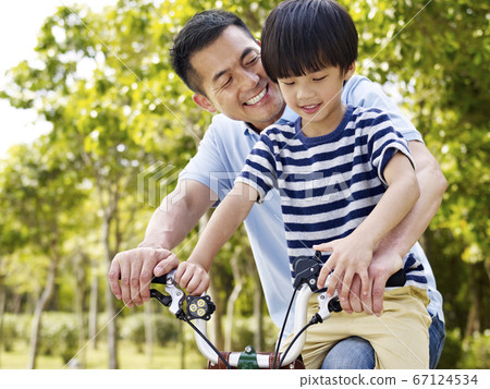 asian father and son enjoying biking outdoors 67124534