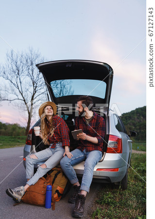 Couple sit on the trunk of car and wonder at photo on tablet 67127143