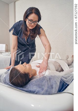 Careful beautician preparing her client for the floating procedure Careful beautician preparing her client for the floating procedure 67127392