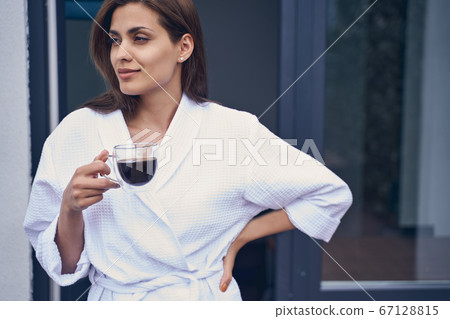 Attractive young woman drinking coffee on balcony 67128815