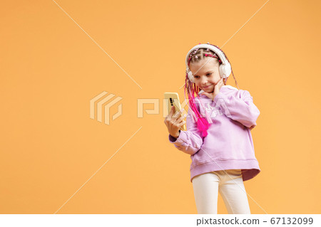 Pretty modern girl with pink dreadlocks in headphones smiling and making selfie on smartphone isolated over yellow 67132099