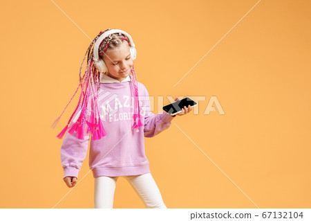 Pretty modern girl with pink dreadlocks in headphones smiling and making selfie on smartphone isolated over yellow Pretty modern girl with pink dreadlocks in headphones smiling and making selfie on smartphone isolated over yellow 67132104