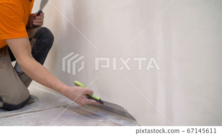 Worker puts putty on the tool. Close-up of a woman's hand with a metal spatula for applying stucco on the wall 67145611