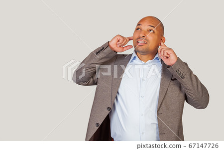 A dark-skinned African-American man, with irritation, plugs his ears with his fingers, not wanting A dark-skinned African-American man, with irritation, plugs his ears with his fingers, not wanting 67147726