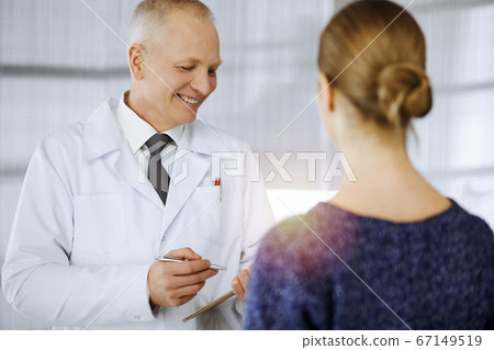 Elderly confident doctor consults woman-patient in sunny clinic. Perfect medical service in medicine 67149519