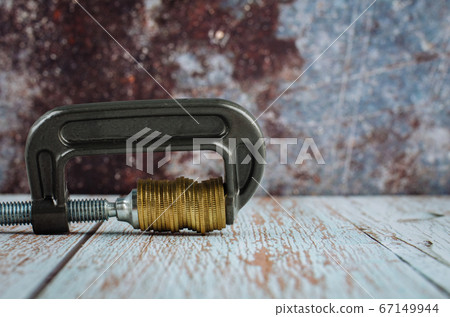 stacking coin squeezing in a G-clamp as a financial crisis concept 67149944