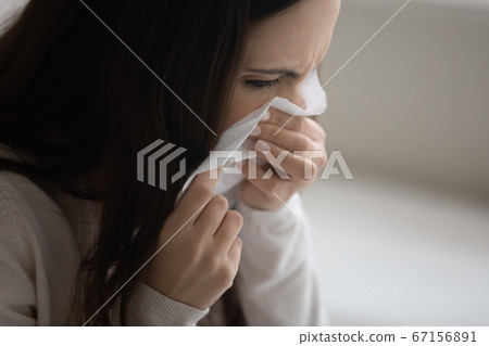 Close up sick young woman blowing nose, holding paper napkin Close up sick young woman blowing nose, holding paper napkin 67156891