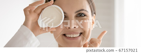 Close up smiling woman holding cream jar, enjoying skincare routine 67157021