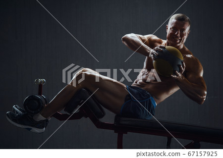 Fitness man pumping up abs muscles in gym 67157925