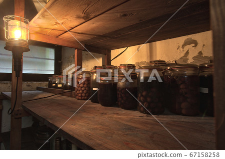Jars with pickled vegetables, fruity compotes and jams in abandoned basement with a light hanging Preserved food in a dark cellar Jars with pickled vegetables, fruity compotes and jams in abandoned basement with a light hanging Preserved food in a dark cellar 67158258