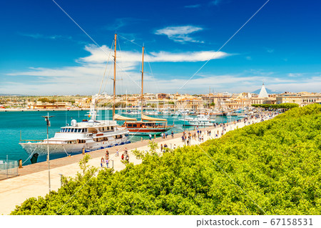 Beautiful view of the harbor in Syracuse with people walking along the promenade Beautiful view of the harbor in Syracuse with people walking along the promenade 67158531