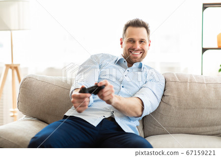 Young man sitting on couch playing video games Young man sitting on couch playing video games 67159221