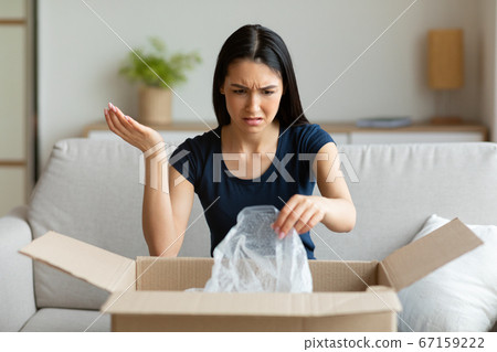 Discontented Girl Unpacking Box Receiving Wrong Parcel Sitting At Home 67159222