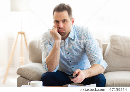 Bored man watching TV at home, holding remote control Bored man watching TV at home, holding remote control 67159254