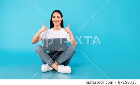 Happy lady sitting with laptop showing thumbs up 67159315