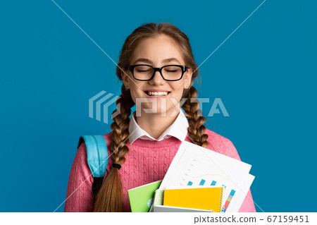 Pleasure of excellent test results. Girl with closed eyes holds notebooks and books 67159451