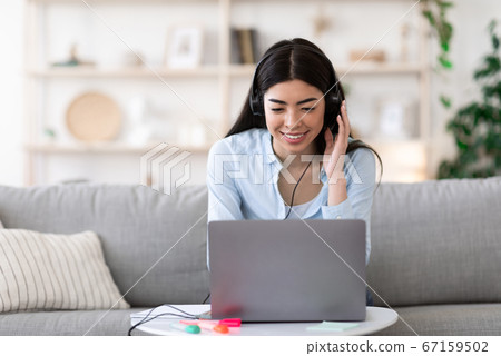Webinar. Smiling asian girl studying online with laptop and headset at home 67159502