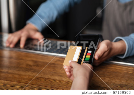 Fast payment for drinks. Girl uses credit card, barman holds terminal on bar counter Fast payment for drinks. Girl uses credit card, barman holds terminal on bar counter 67159503