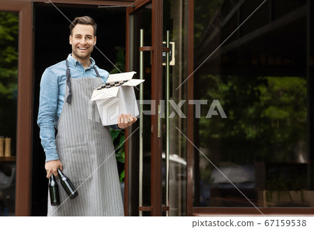 Preparation for party in pub. Smiling handsome barman carries box with beer and bottles in hands Preparation for party in pub. Smiling handsome barman carries box with beer and bottles in hands 67159538