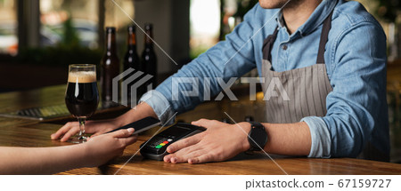 Bartender offers to pay the bill with termina, girl holds phone in interior of pub Bartender offers to pay the bill with termina, girl holds phone in interior of pub 67159727