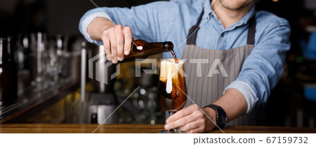 Client order at pub. Bartender pours dark beer in glass at bar Client order at pub. Bartender pours dark beer in glass at bar 67159732