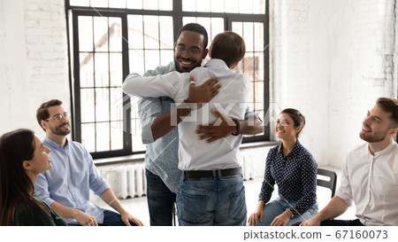 African and Caucasian men embracing during group therapy counseling session 67160073