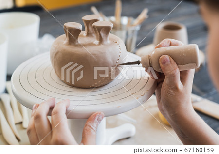 Closeup of bottom of mug, which is being decorated in ceramic studio. Female professional hands making clay dots or drops on the surface of vase by special squeezing tool. 67160139