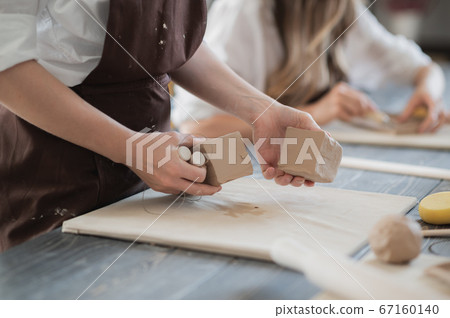 White clay preparation for work. Cutting layers of clay pieces for sculpting in the workshop of a potter Close-up. Raw bar of clay on the old wooden table in pottery. 67160140