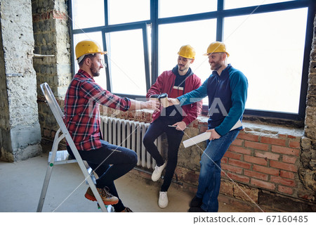 Three young architects in protective helmets clinking with glasses of coffee 67160485
