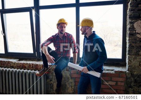 Young confident engineer in protective helmet consulting his colleague Young confident engineer in protective helmet consulting his colleague 67160501