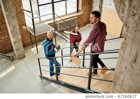 Young architect with rolled paper discussing details of quality with colleagues Young architect with rolled paper discussing details of quality with colleagues 67160617