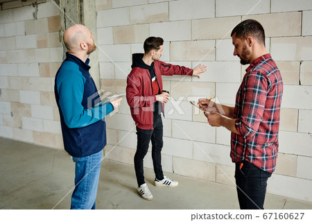 Young contractor with drink touching white brick while standing by wall 67160627