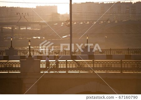 Two young intercultural persons in activewear jogging along bridge by riverside Two young intercultural persons in activewear jogging along bridge by riverside 67160790
