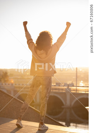 Young ecstatic sportswoman in leggins and hoodie keeping her arms raised Young ecstatic sportswoman in leggins and hoodie keeping her arms raised 67160806