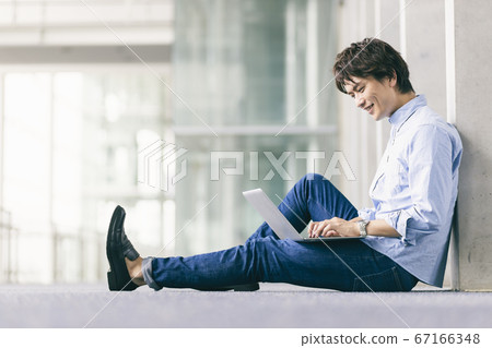 A man sitting on the floor and using a computer 67166348