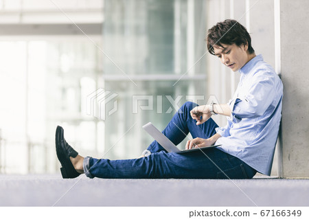 A man sitting on the floor and using a computer 67166349