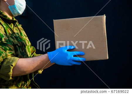 the military delivers food to your home. assistance to pensioners, the poor and the population. a courier in rubber gloves holds a box on a black background. 67169022